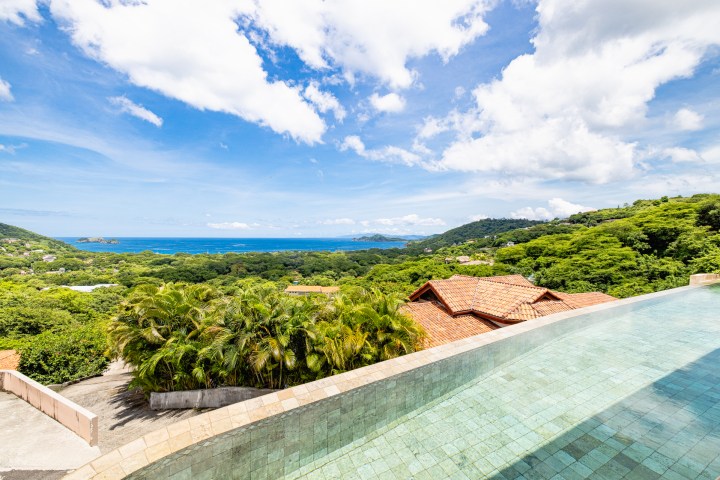 Infinity pool overlooking lush hills and ocean under a partly cloudy sky.
