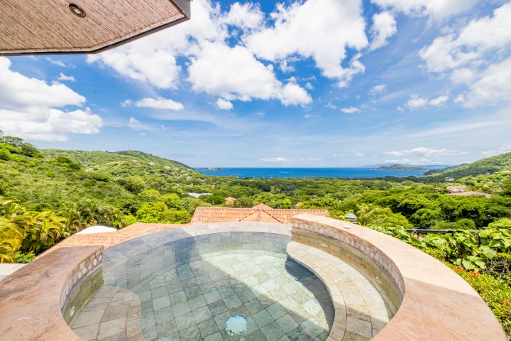 Infinity pool overlooking lush hills and ocean under a cloudy sky.