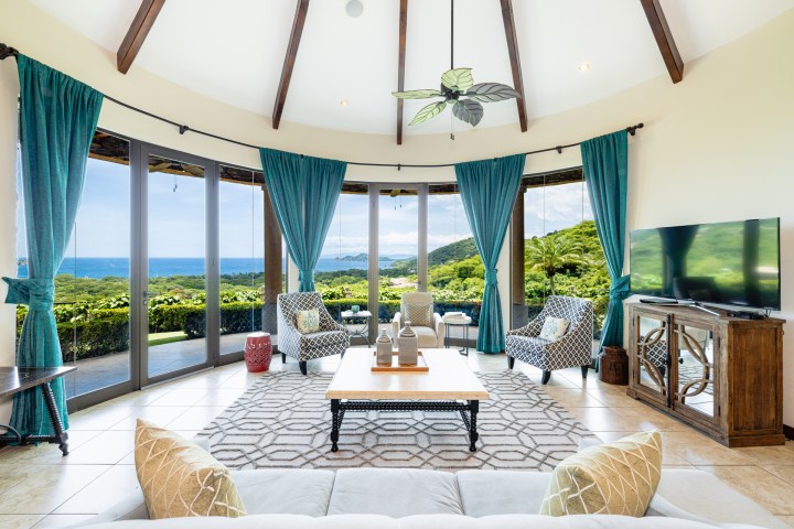 Spacious room with large windows, ocean view, modern decor, and teal curtains.