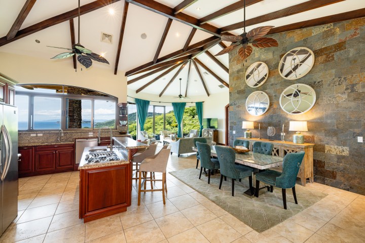 Spacious kitchen and dining area with vaulted ceiling, wooden beams, tropical decor, and large windows.