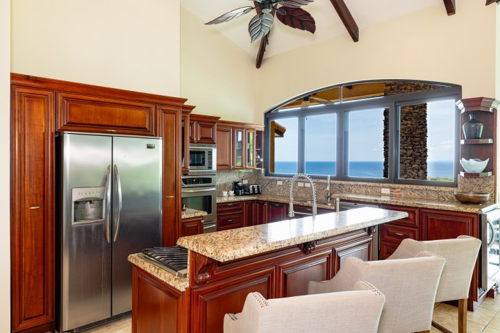 Spacious kitchen with wooden cabinets, granite countertops, and ocean view through large window.
