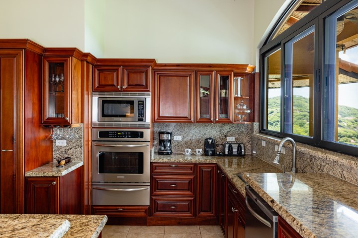 Modern kitchen with wooden cabinets, appliances, granite countertops, and a large window view.