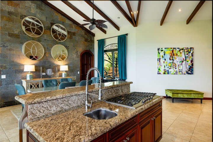 Modern kitchen and living area with stone wall, mirrors, and abstract painting on white wall.