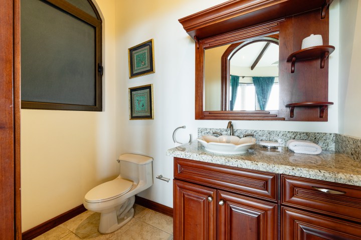 Bathroom with wooden vanity, granite countertop, toilet, and framed pictures on wall.