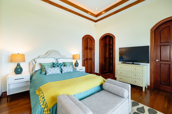 Bedroom with a bed, TV, and wooden doors, featuring blue and yellow accents.