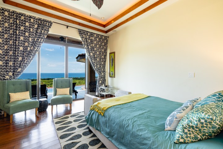 Ocean-view bedroom with teal bedding and patterned curtains.