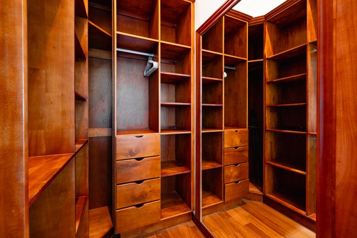 Empty wooden walk-in closet with shelves, drawers, and hanging rod.