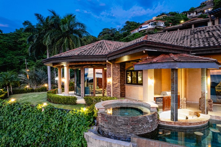 Luxury villa with pool and lush landscaping at sunset.