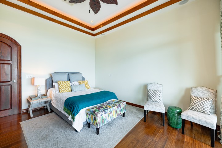 Bright bedroom with a bed, two chairs, wooden floor, and a decorative leaf ceiling.