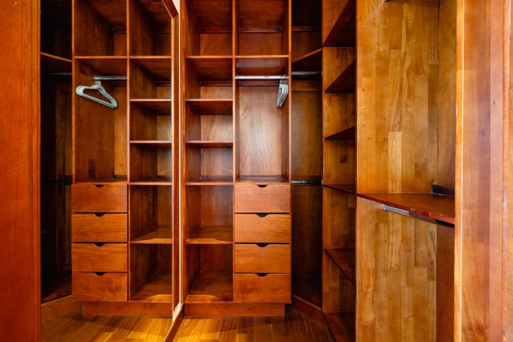 Wooden walk-in closet with shelves, drawers, and hangers.