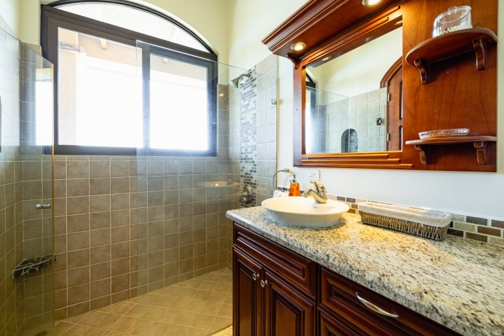 Bathroom with granite countertop, wooden cabinets, and tiled walk-in shower.