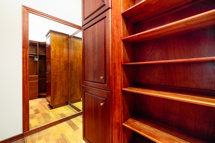 Wooden closet with shelves and mirrored doors on a wooden floor.