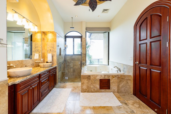 Luxury bathroom with stone tiles, a double vanity, bathtub, and a large glass shower.