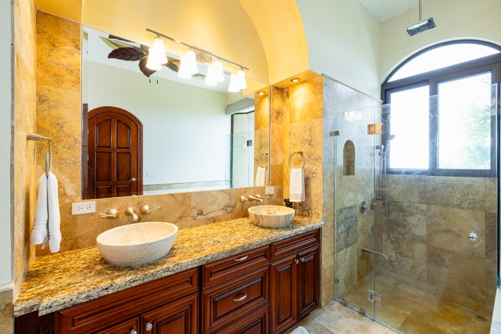 Elegant bathroom with marble sink, wood cabinets, and glass shower.