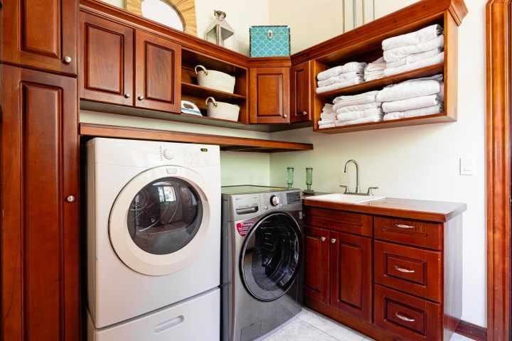 Laundry room with stacked washer and dryer, wooden cabinets, and sink.