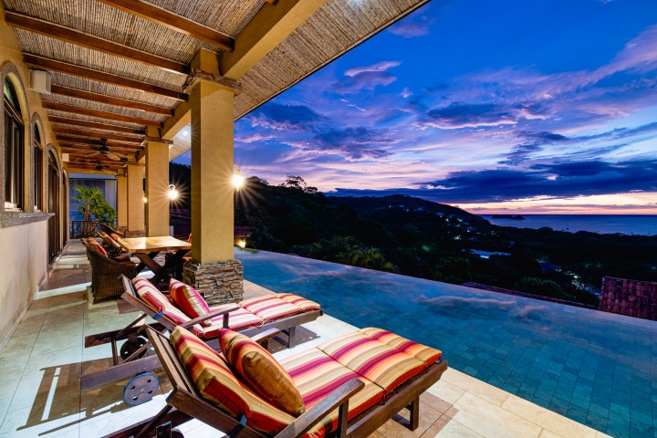 Patio with lounge chairs overlooking an infinity pool at sunset.