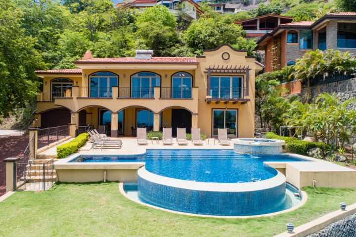 Luxury villa with pool and patio, surrounded by greenery on a hillside.