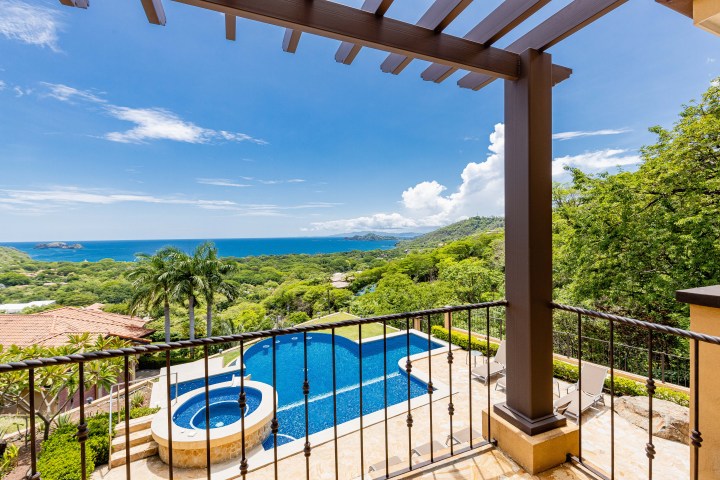 Balcony view of a pool, palm trees, and ocean with clear blue sky in the background.