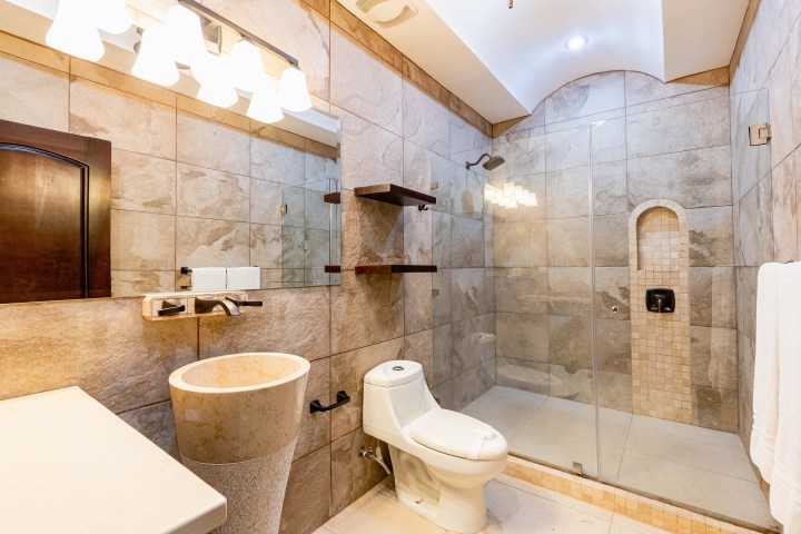 Modern bathroom with a glass shower, stone tiles, pedestal sink, and toilet.