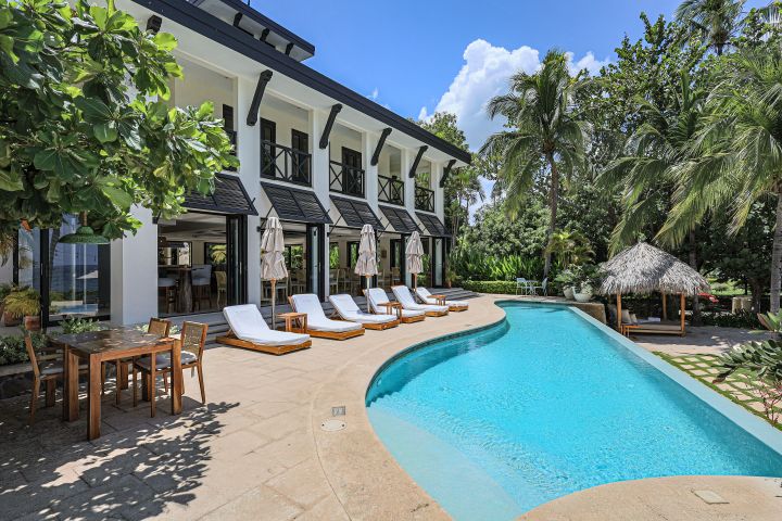 Tropical villa with pool, lounge chairs, and palm trees on a sunny day.