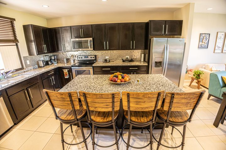 Modern kitchen with dark cabinets, granite island, and wooden bar stools.