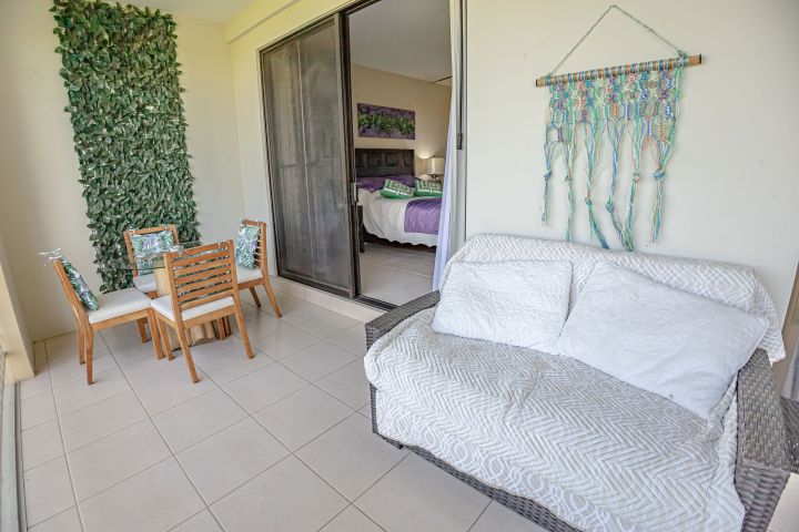 Patio with white sofa, dining set, wall greenery, and macramé, bedroom visible through sliding doors.