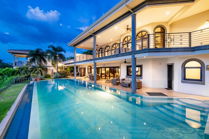 Luxurious villa with an illuminated pool and balconies at dusk.