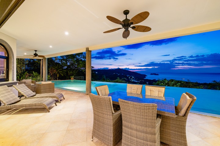 Outdoor patio with wicker furniture and infinity pool overlooking ocean at sunset.
