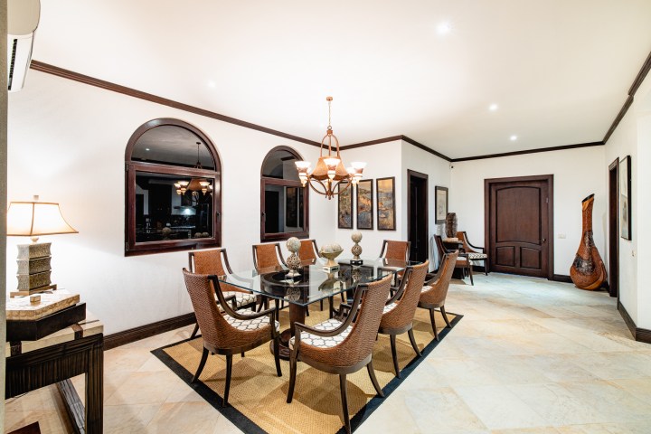 Elegant dining room with a glass table, wicker chairs, and decorative lighting.