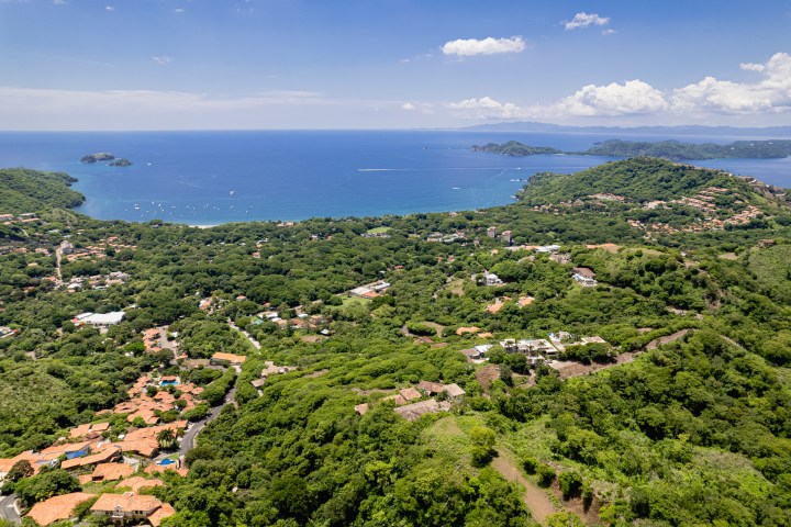 Aerial view of a lush coastal landscape with scattered houses and blue ocean.
