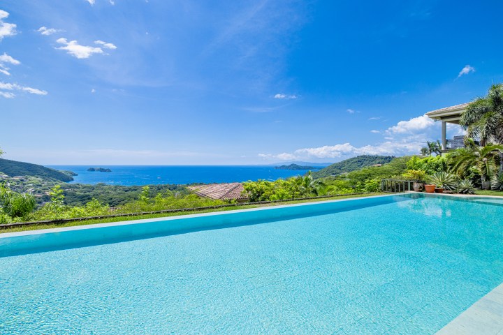 Infinity pool overlooking ocean and hills under a clear blue sky.