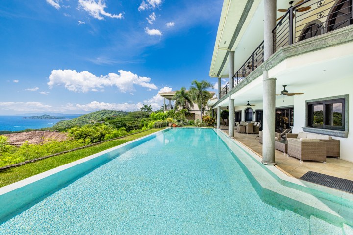 Infinity pool at luxury villa overlooking ocean and lush green hills.