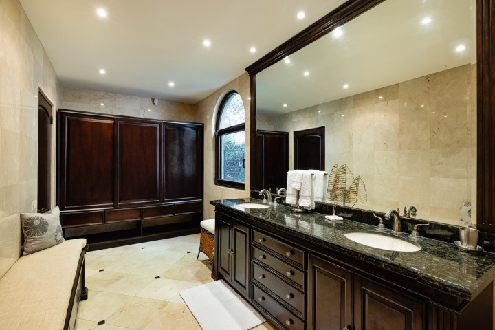 Elegant bathroom with double vanity, large mirror, dark wood cabinets, and cream tiles.