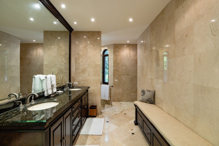 Luxurious bathroom with double sink, large mirror, marble walls, and a cushioned bench.