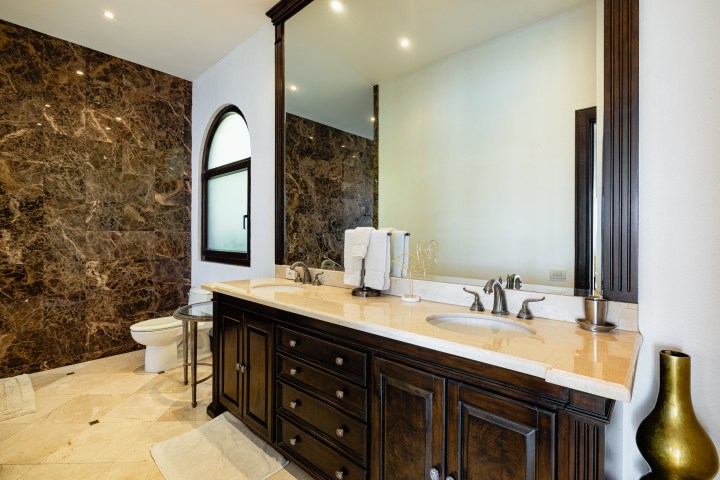 Luxurious bathroom with marble walls, wooden vanity, large mirror, and toilet.