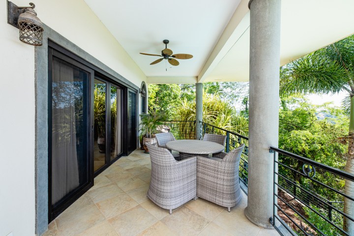 Covered balcony with rattan furniture set, ceiling fan, and tropical view.