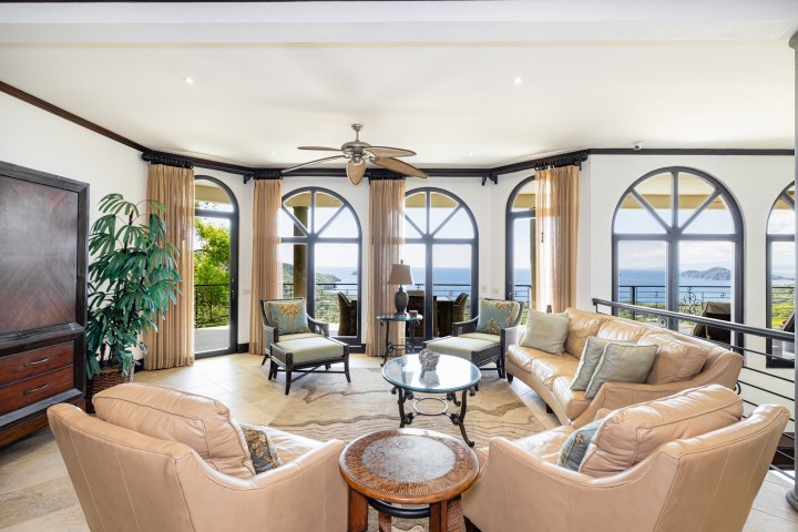 Elegant living room with tan sofas and a sea view through arched windows.