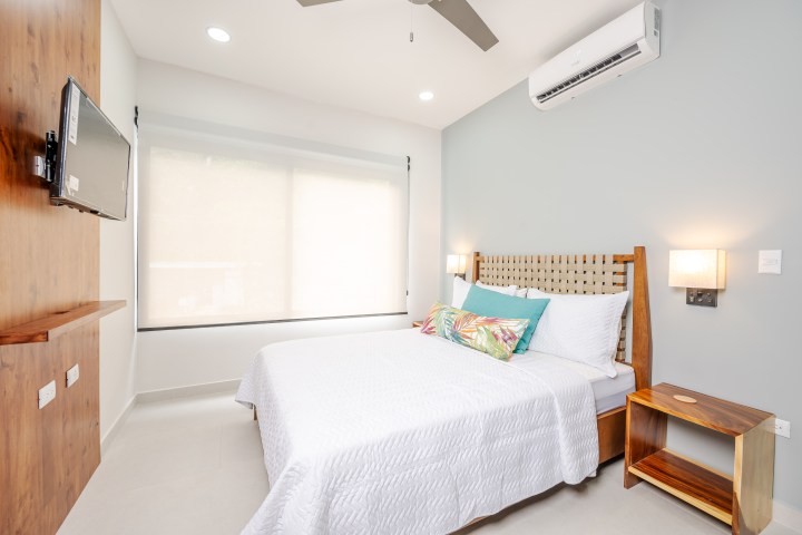Minimalist bedroom with bed, TV, window, ceiling fan, and air conditioner.