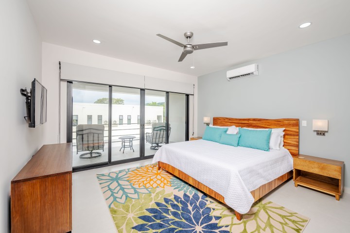 Modern bedroom with a bed, colorful rug, TV, and glass doors leading to a balcony.