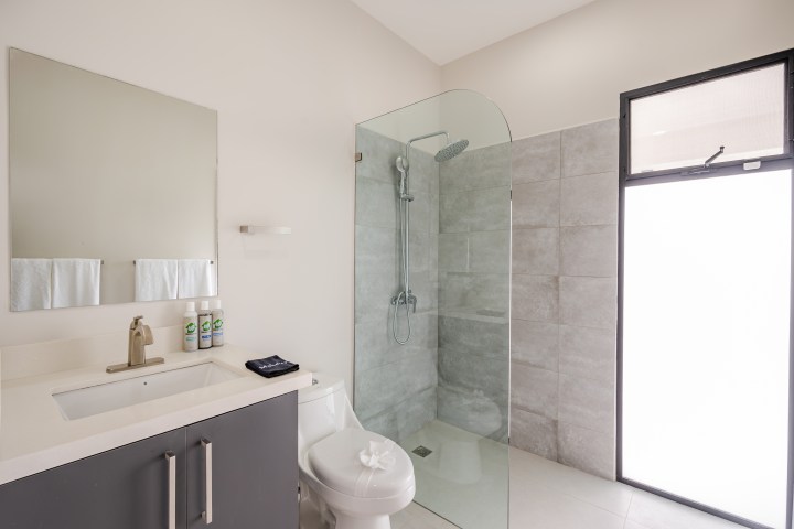 Modern bathroom with glass shower, large mirror, sink, and toilet.
