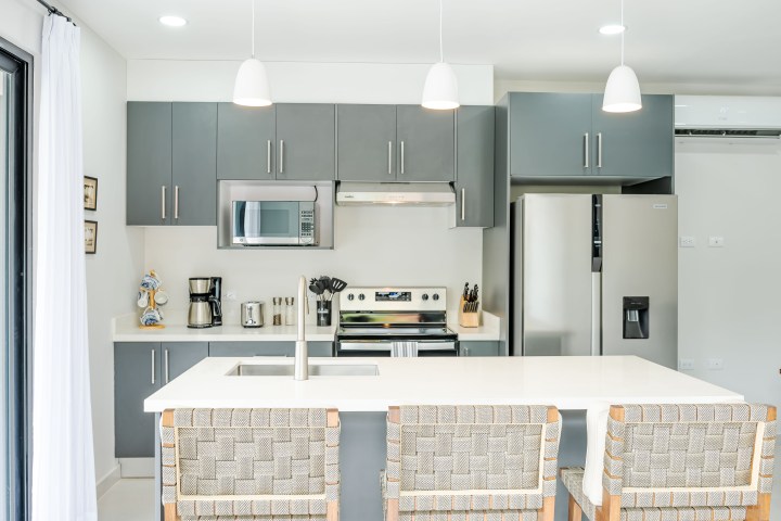 Modern kitchen with gray cabinets, stainless steel appliances, and a white island with woven chairs.