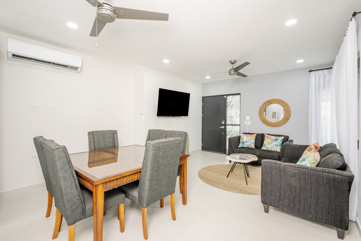Modern living room with gray sofas, dining table, TV, and ceiling fans.