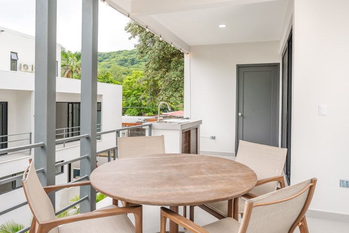 Outdoor patio with round table and chairs, overlooking modern buildings and greenery.