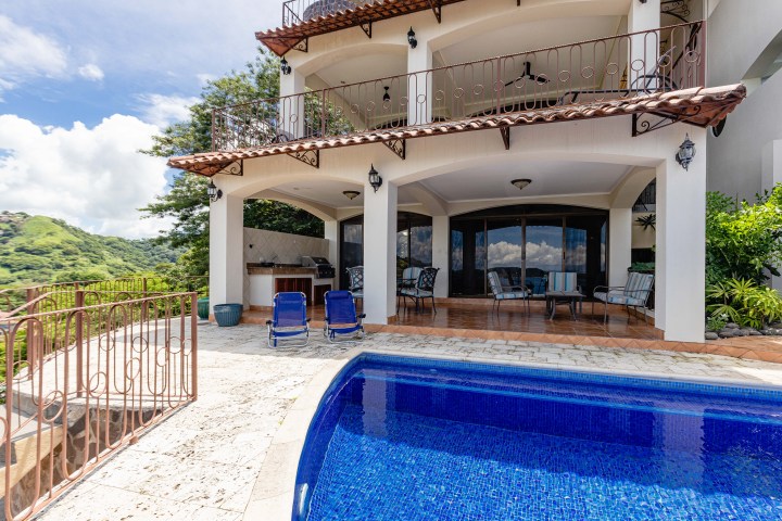 Luxurious house with a pool, patio seating, and scenic mountain views.