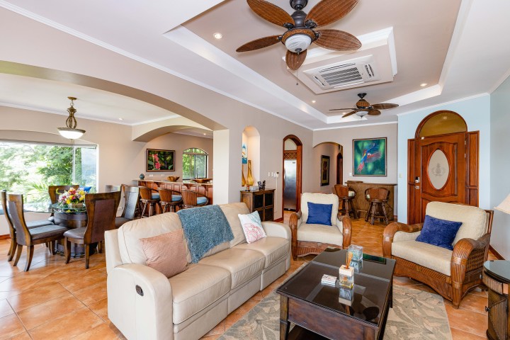 Spacious living room with beige sofas, ceiling fans, and dining area with bay window view.