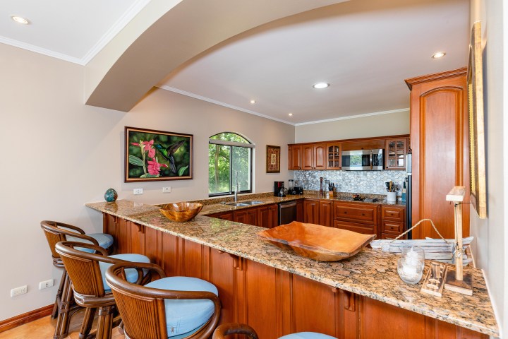 Kitchen with wooden cabinets, granite countertops, bar stools, and a large window view.