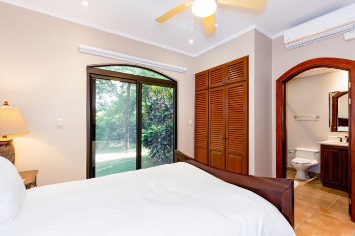 Bedroom with bed, sliding glass doors, fan, closet, and attached bathroom.