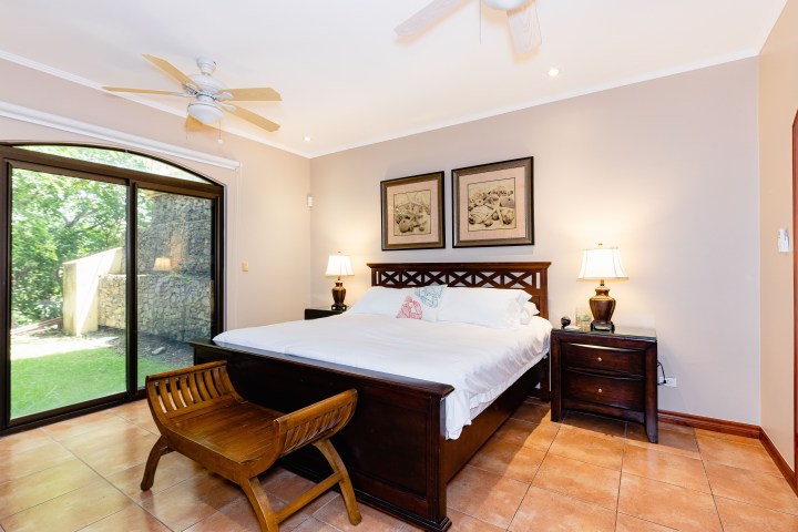 Cozy bedroom with bed, wooden furniture, lamps, and sliding glass door to a grassy backyard.