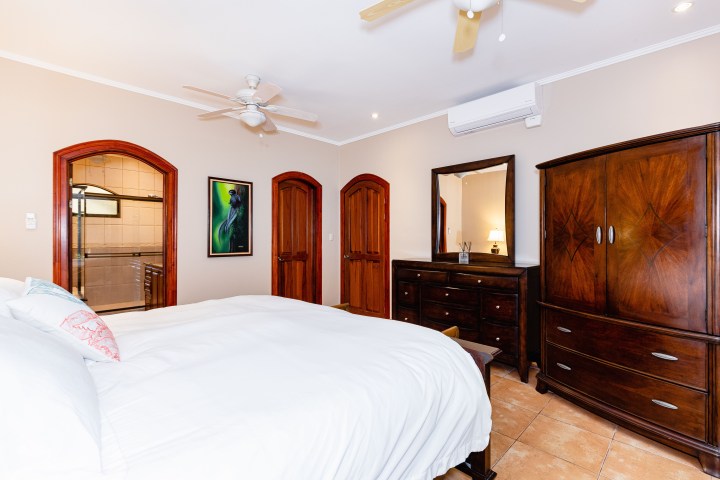 Bedroom with white bedding, dark wood furniture, ceiling fan, and open door to bathroom.