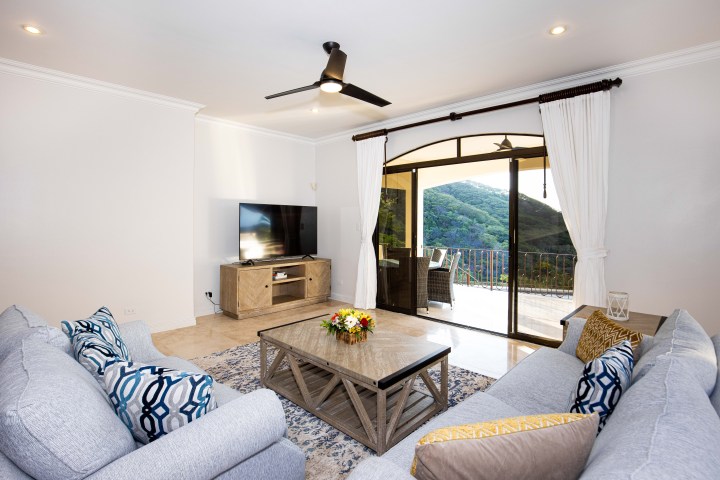 Modern living room with sofas, TV, ceiling fan, and balcony view.